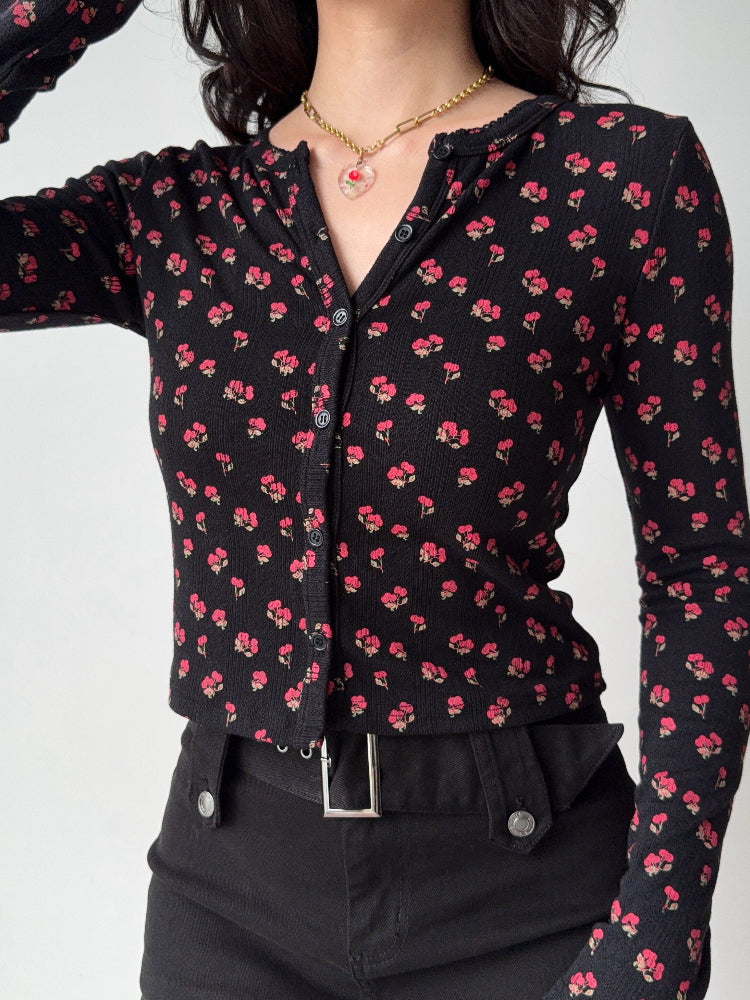 Close-up of a woman wearing a black long-sleeve cardigan with a small pink floral print.