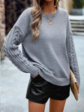 Close-up of a grey knit sweater with intricate cable knit detailing on the sleeves
