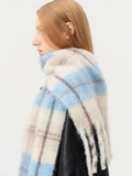 Close-up of a woman wearing a fuzzy plaid scarf with blue and beige squares and a fringed hem.