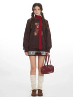 Woman wearing a brown oversized knit sweater with a teddy bear graphic and red scarf.