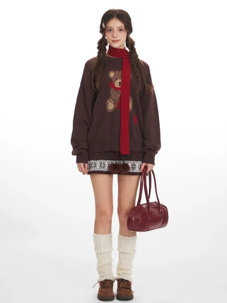 Woman wearing a brown oversized knit sweater with a teddy bear graphic and red scarf.