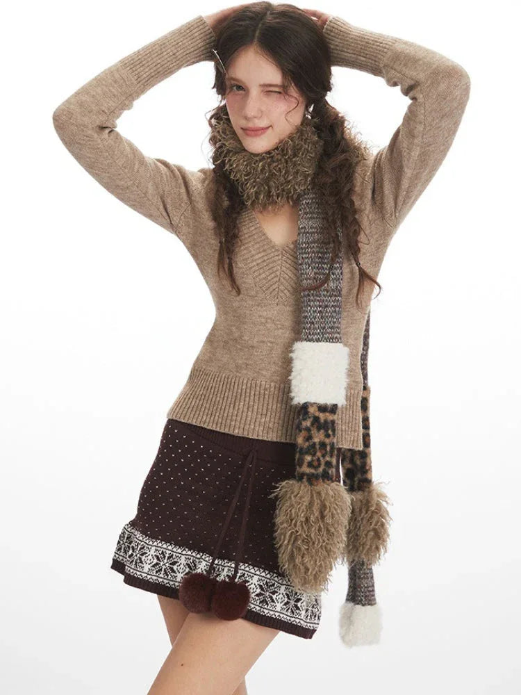 Woman in a beige V-neck knit sweater and brown patterned skirt, posing with hands behind head, wearing a patterned scarf with faux fur trim.