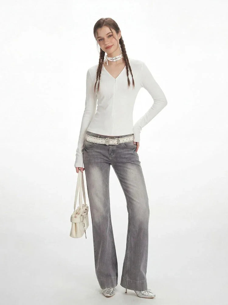 Full body shot of a woman in a white long-sleeve top and distressed grey jeans.
