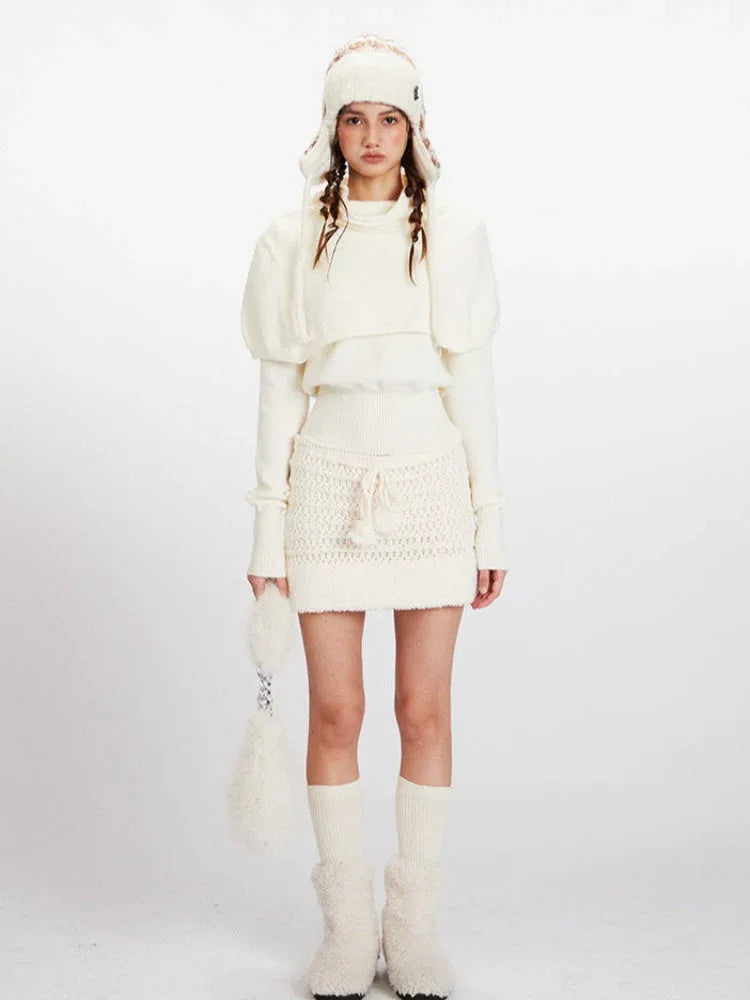 Woman wearing a cream knit turtleneck sweater with puffed sleeves over a cream knit mini skirt with a drawstring waist.