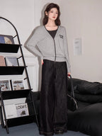 Woman wearing a grey V-neck knit cardigan with contrast trim and embroidered graphic detail with a dark top and wide-leg jeans
