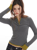 Woman posing with a grey long-sleeve Henley top with contrast green cuffs and hem and dark wash baggy jeans