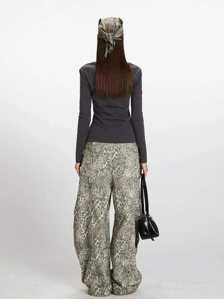 Back view of a woman wearing a dark grey long-sleeve ribbed knit top with a square neckline and buttoned placket, paired with grey leopard print wide-leg cargo pants and a black handbag.