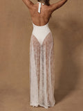 Back view of a woman wearing a white one-piece swimsuit and a sheer white lace maxi skirt.