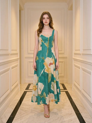 Woman wearing a green midi dress with a large floral print, standing in a hallway.