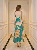 Back view of a woman in a green midi dress with a floral print, standing in a hallway.