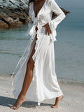 Woman walking on a sandy beach wearing a white sheer chiffon maxi dress with ruffle trim and tie front