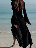Woman walking away from the camera on a sandy beach wearing a black sheer chiffon maxi dress with flared sleeves