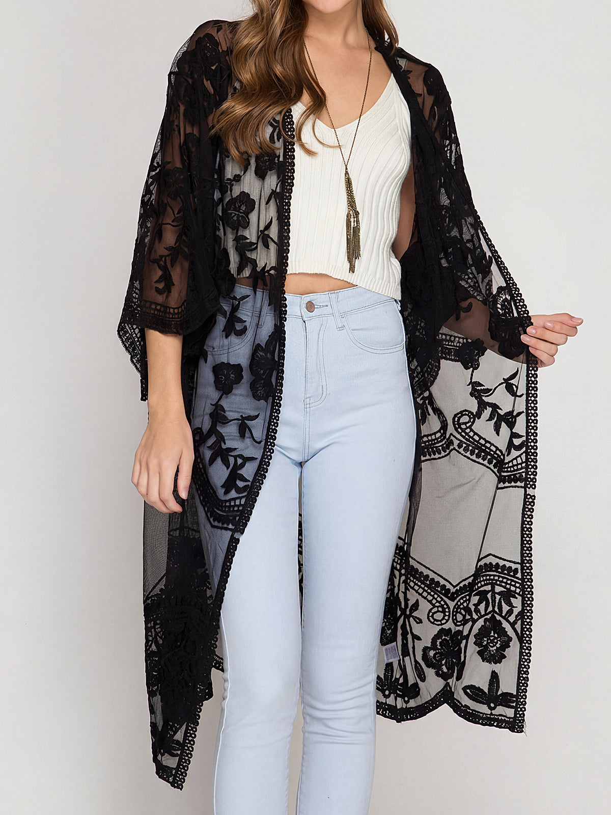 Woman wearing a black lace duster over a white top and light blue jeans