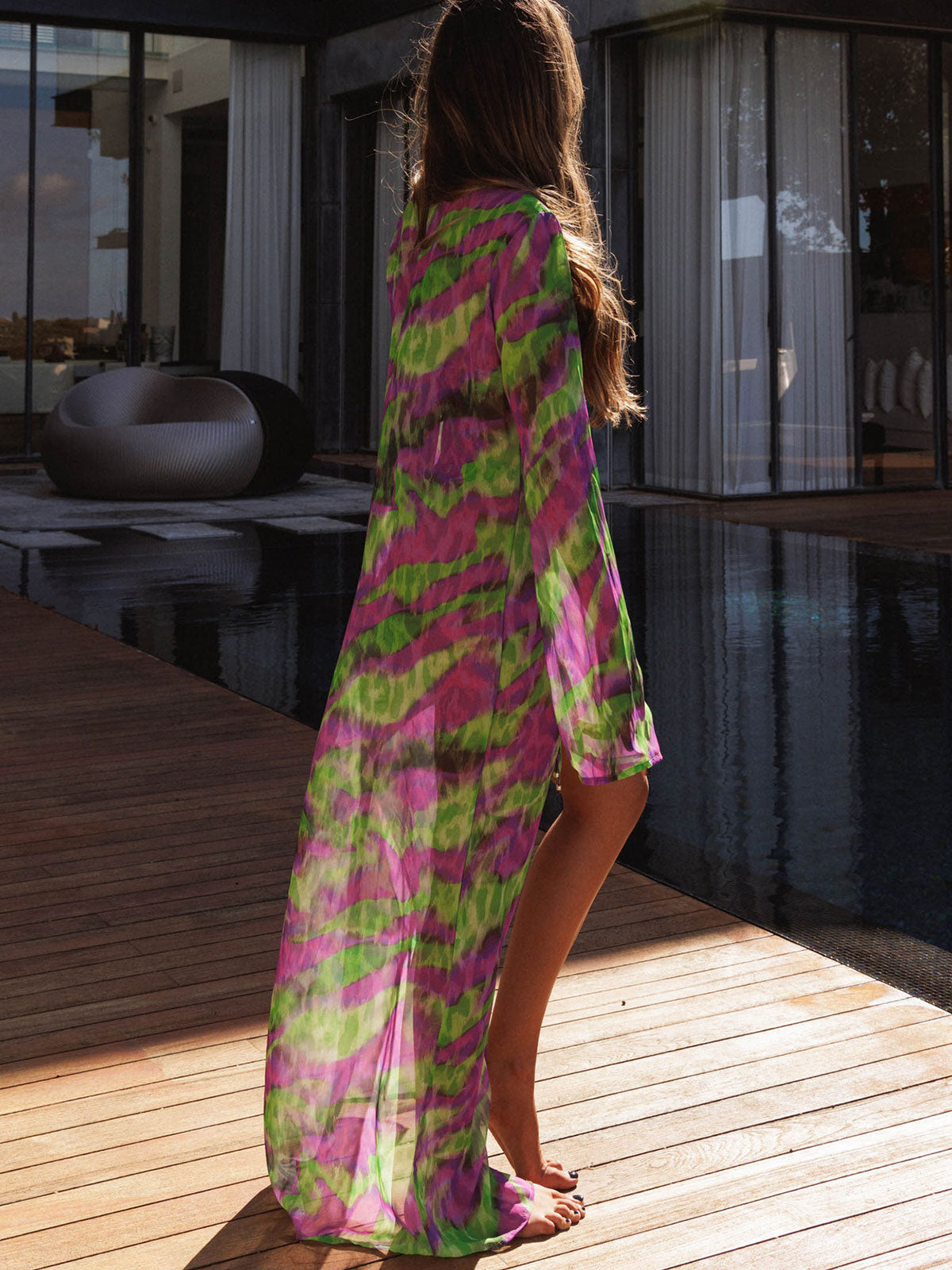 Back view of a woman in a long, sheer tie-dye duster with split sides.