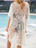 Rear view of a woman wearing a white lace beach cover-up over a black bikini, standing by a pool
