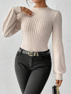 Woman styling a cream ribbed knit bodysuit with black jeans and a gold buckle belt