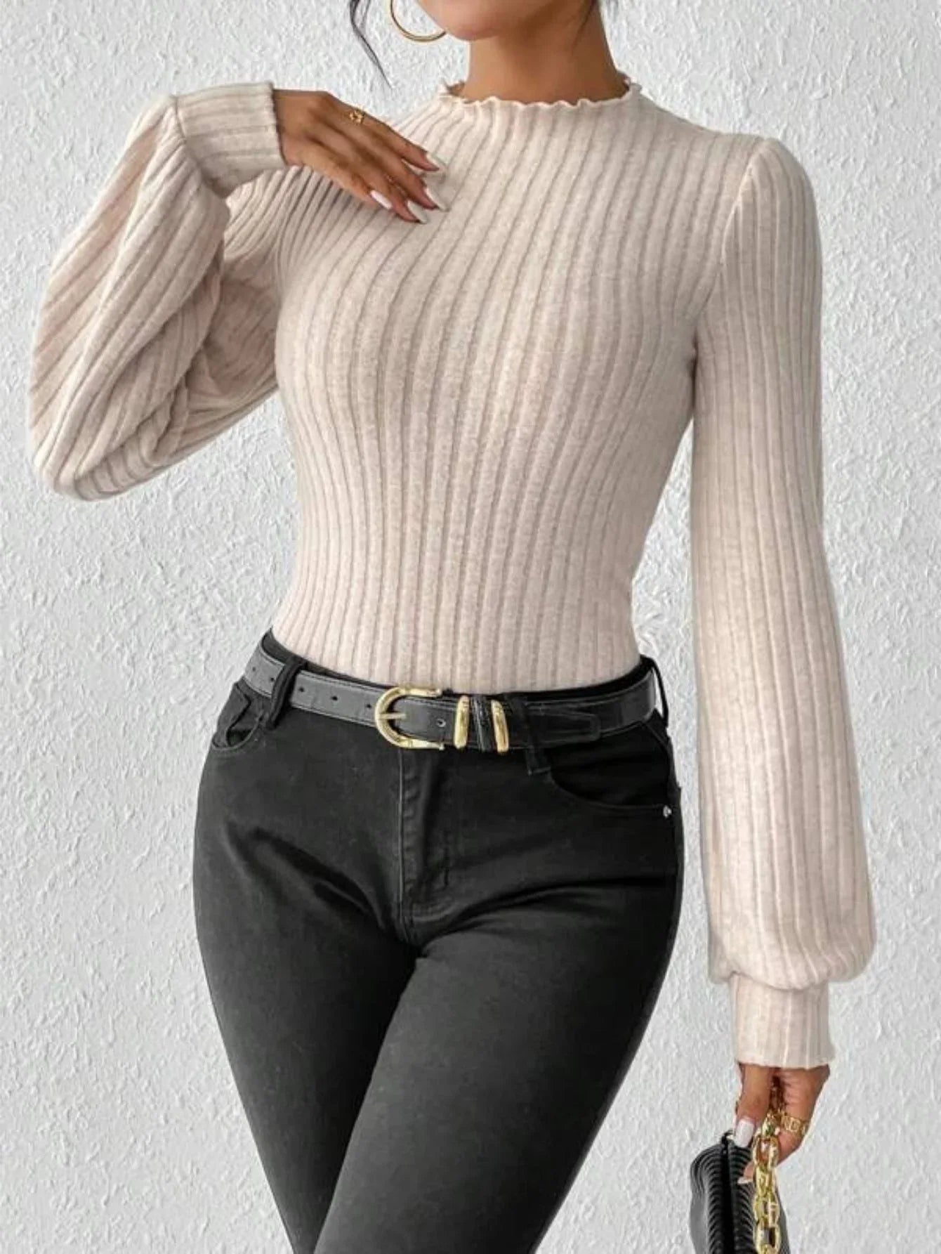 Woman styling a cream ribbed knit bodysuit with black jeans and a gold buckle belt