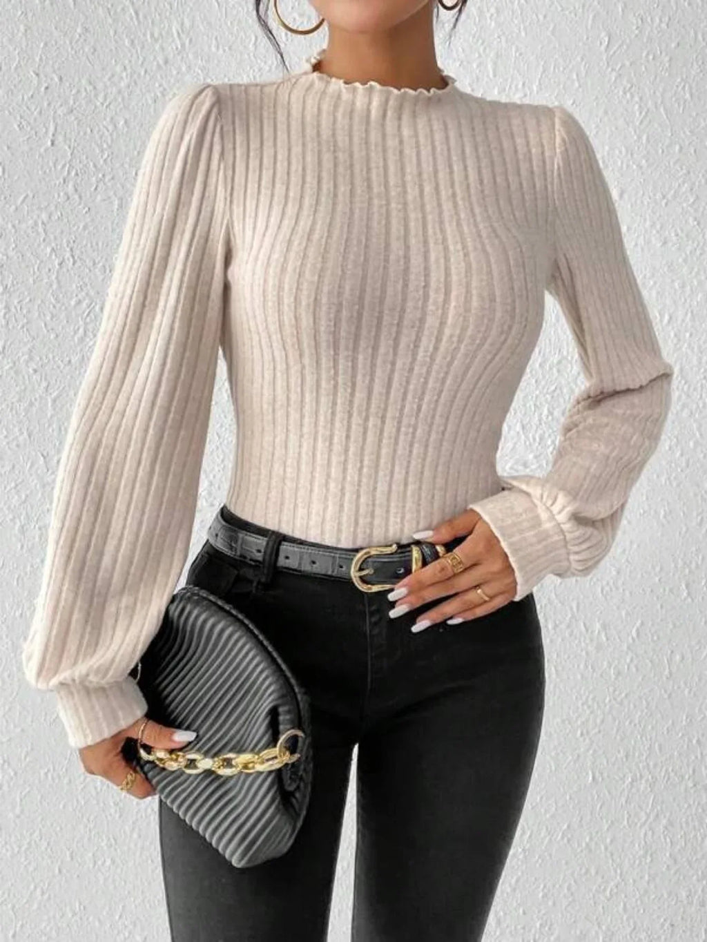 Woman holding a grey clutch bag while wearing a cream ribbed knit bodysuit and black jeans