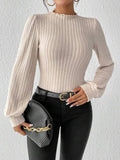 Woman holding a grey clutch bag while wearing a cream ribbed knit bodysuit and black jeans