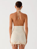 Back view of a woman wearing a cream knit halter mini dress with an open back and beaded hem