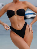 Model wearing a black strapless bikini with gold hardware on a beach