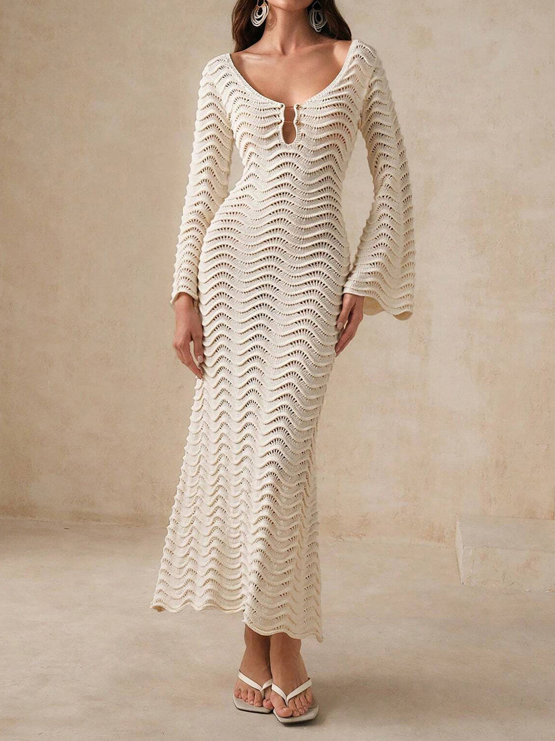 Woman wearing a cream-colored, long-sleeved, midi-length knit dress with a wave pattern and bell sleeves.