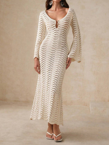 Woman wearing a cream-colored, long-sleeved, midi-length knit dress with a wave pattern and bell sleeves.