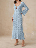 Woman wearing a light blue, long-sleeved, midi-length knit dress with a wave pattern and bell sleeves.