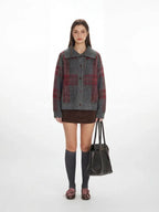 Woman wearing a grey and red plaid collared knit jacket with a brown skirt and grey knee-high socks.
