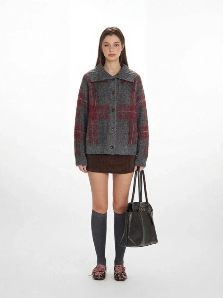 Woman wearing a grey and red plaid collared knit jacket with a brown skirt and grey knee-high socks.