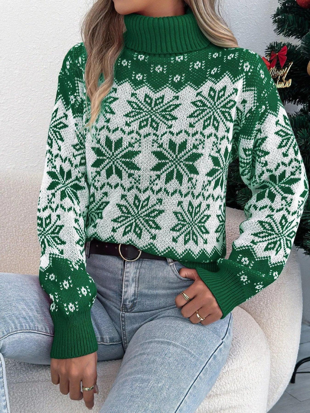 Woman sitting on a chair wearing a green and white snowflake pattern turtleneck sweater, front view.
