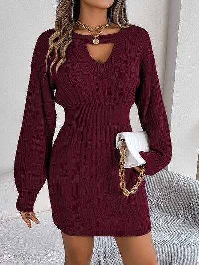 Woman wearing a burgundy cable knit mini dress with a cutout V-neck and bishop sleeves, holding a white clutch.