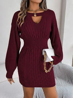 Woman wearing a burgundy cable knit mini dress with a cutout V-neck and bishop sleeves, holding a white clutch.