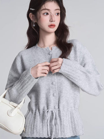 Woman wearing a light gray knit cardigan with a drawstring waist.