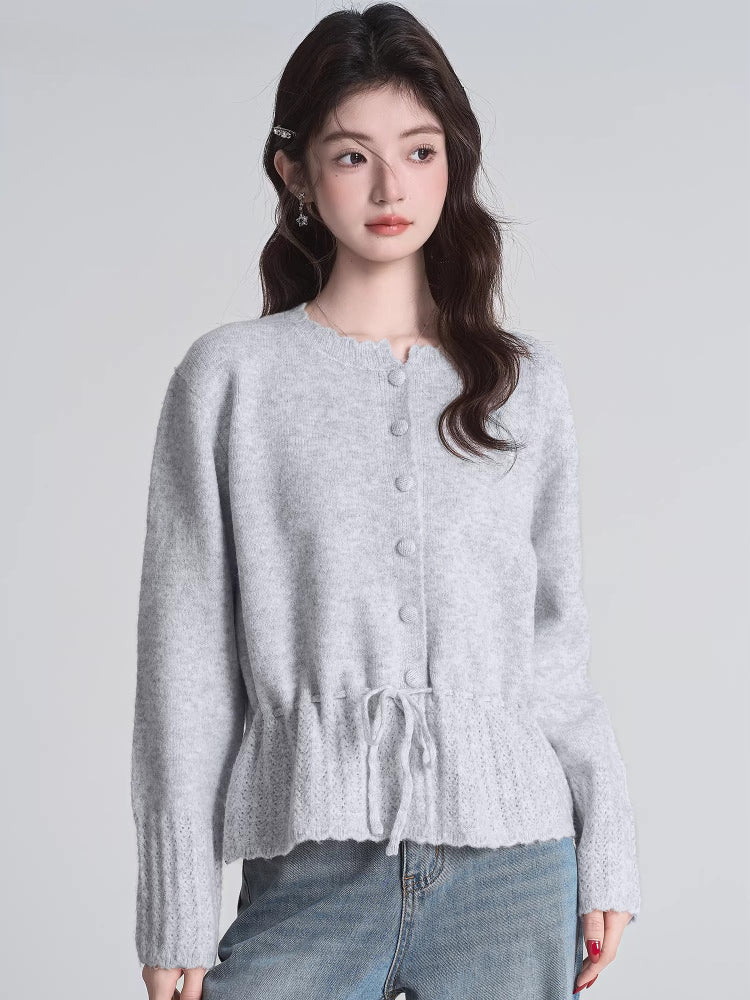 Woman wearing a light gray knit cardigan with a drawstring waist.
