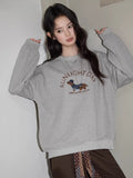 A woman poses in a gray crew neck sweatshirt with a dachshund graphic.