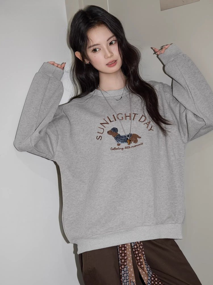 A woman poses in a gray crew neck sweatshirt with a dachshund graphic.