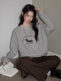 A woman sits on the floor wearing a gray crew neck sweatshirt with a graphic print.