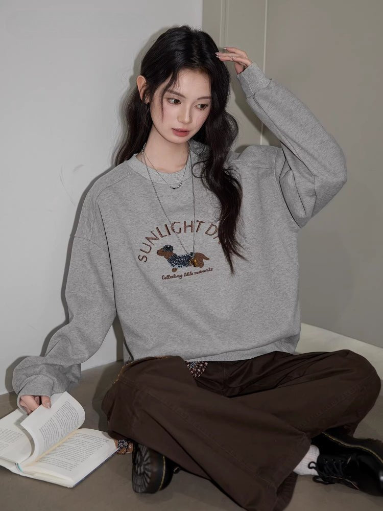 A woman sits on the floor wearing a gray crew neck sweatshirt with a graphic print.