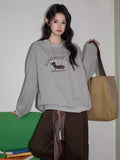 A woman wearing a gray crew neck sweatshirt with a graphic of a dachshund and the text 