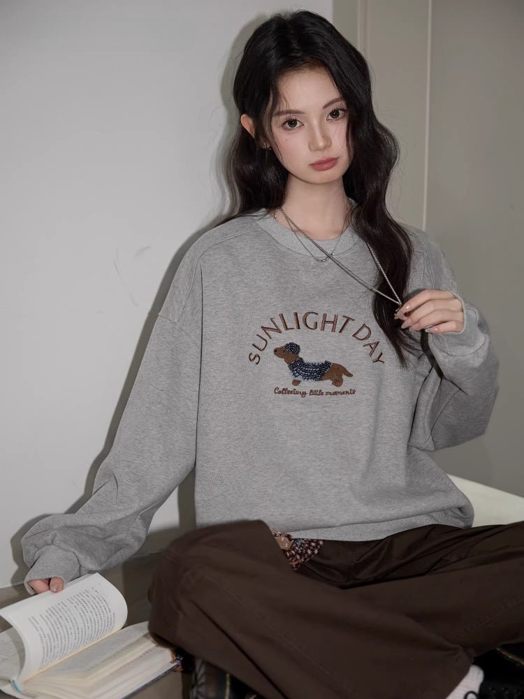 A woman wearing a gray crew neck sweatshirt with a graphic of a dachshund and the text "SUNLIGHT DAY".