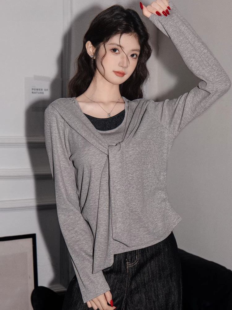 Woman posing with an arm raised, wearing a grey knit top with a draped neckline and layered effect.