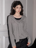 Woman wearing a grey long-sleeve knit top with a draped neckline and layered look, paired with dark wash wide-leg jeans.
