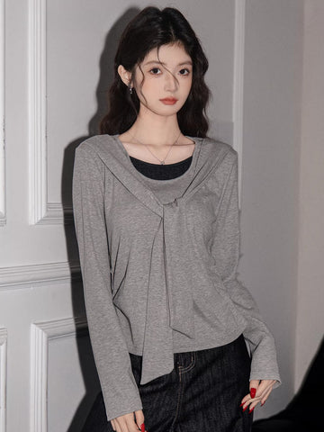 Woman wearing a grey long-sleeve knit top with a draped neckline and layered look, paired with dark wash wide-leg jeans.