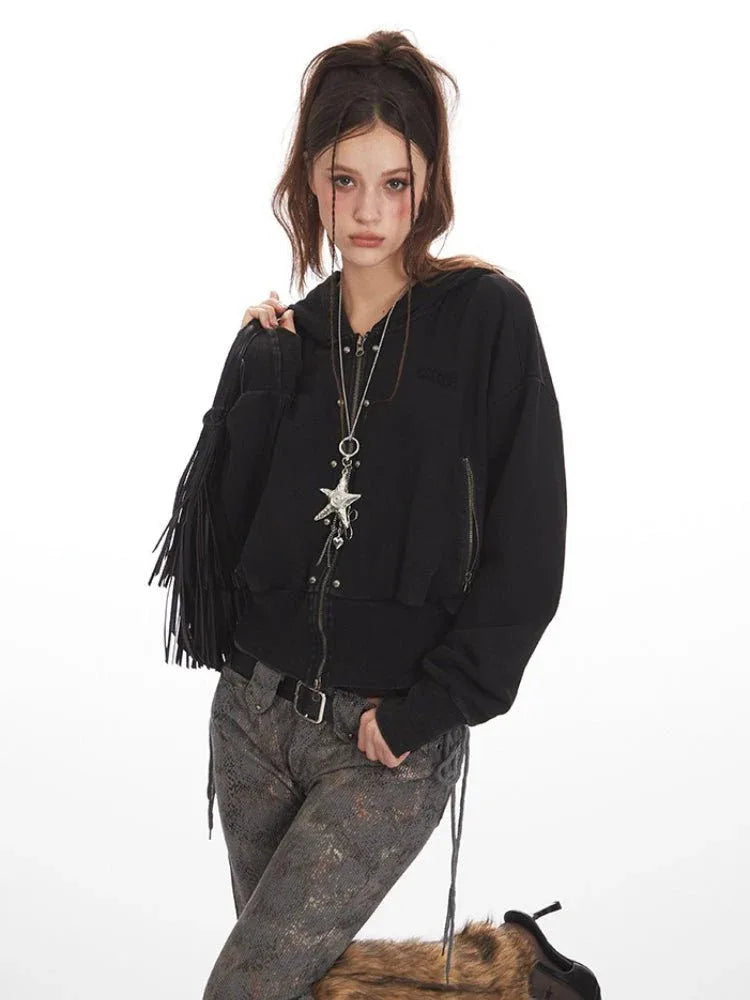 Close-up of a woman in a black cropped hooded zip-up jacket, showing the zipper and star pendant necklace.