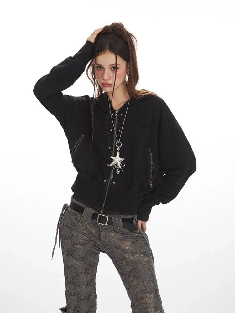 Woman adjusting her hair while wearing a black cropped hooded zip-up jacket and patterned pants.
