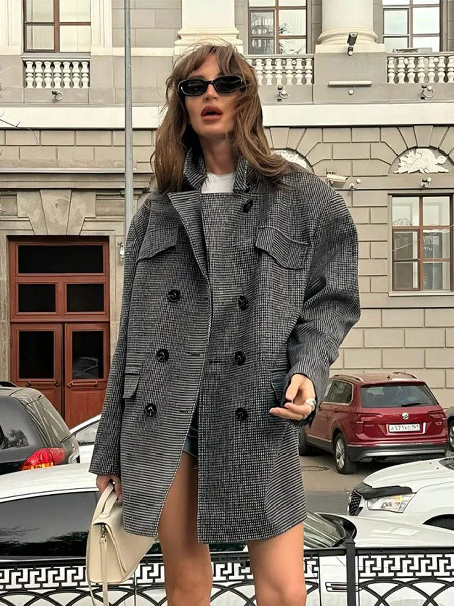 Woman wearing an oversized grey houndstooth double-breasted blazer with peak lapels and flap pockets, paired with a white t-shirt and black shorts. Main image