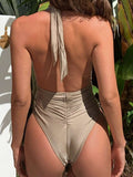 Back view of a woman in a shimmering gold one-piece swimsuit showing ruched detailing and halter tie