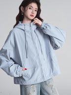 Close-up of a woman in a light blue hooded jacket, showing the zippered front and pockets.