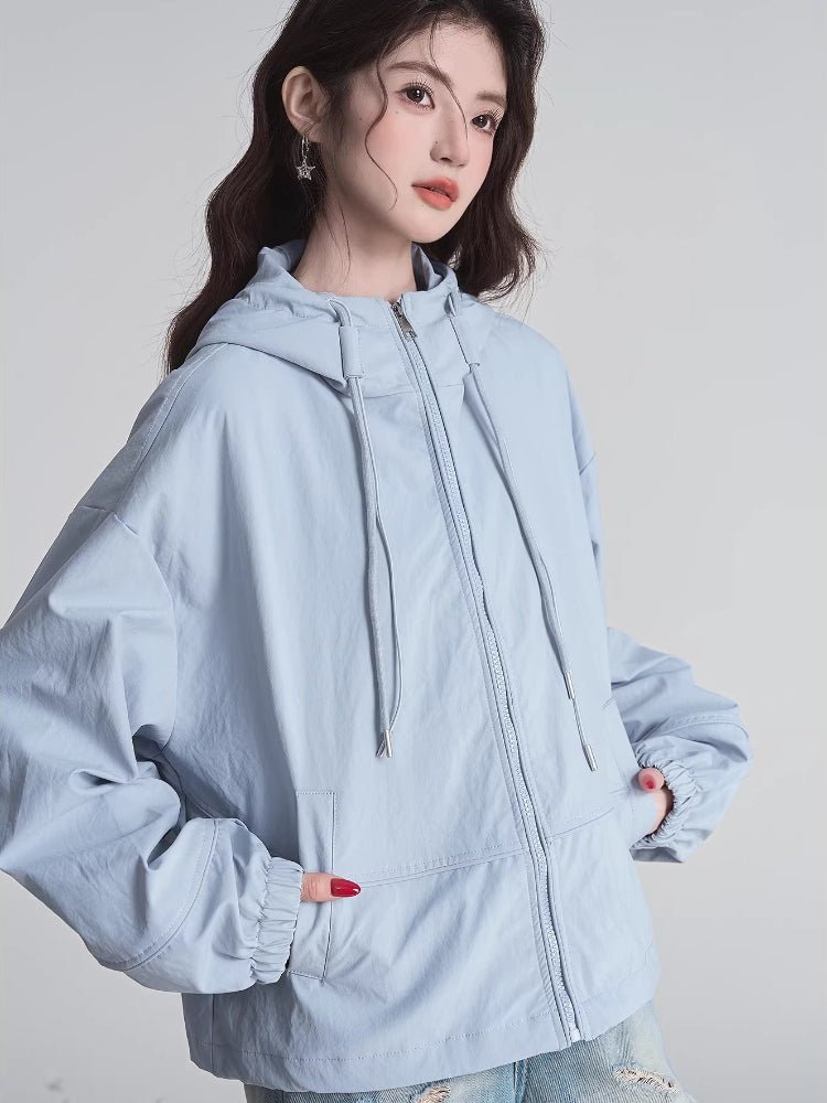 Woman posing with hands in the pockets of her light blue hooded jacket.